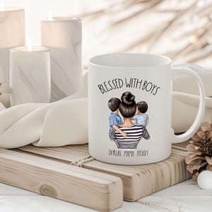 Puede incluir: Taza de cer&aacute;mica blanca con una ilustraci&oacute;n en blanco y negro de una madre con dos ni&ntilde;os. El texto "Blessed with Boys" est&aacute; impreso en negro en la taza. El texto "Oh, how I love my boys!" est&aacute; impreso en negro en la parte inferior de la taza.