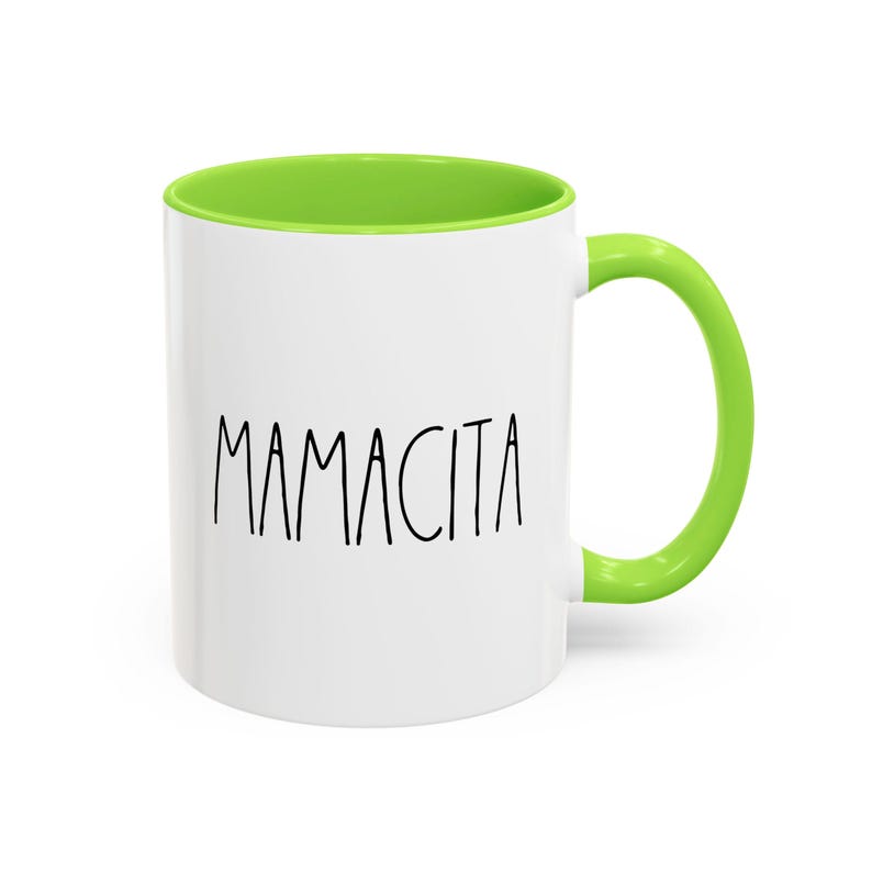 May include: White ceramic mug with a green interior and handle. The word "MAMACITA" is printed in black, handwritten-style font on the front of the mug. The mug is designed for hot beverages.
