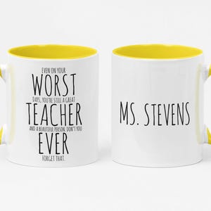 May include: White ceramic mug with a yellow interior and handle. The mug features the text "EVEN ON YOUR WORST DAYS, YOU'RE STILL A GREAT TEACHER AND A BEAUTIFUL PERSON, DON'T YOU EVER FORGET THAT" on one side and "MS. STEVENS" on the other.