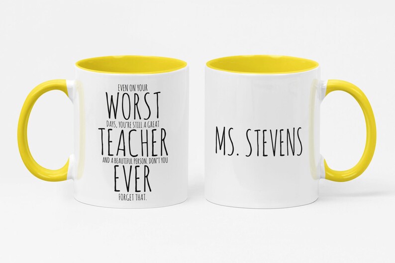 May include: White ceramic mug with a yellow interior and handle. The mug features the text "EVEN ON YOUR WORST DAYS, YOU'RE STILL A GREAT TEACHER AND A BEAUTIFUL PERSON, DON'T YOU EVER FORGET THAT" on one side and "MS. STEVENS" on the other.