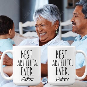 Peut inclure: Deux tasses en c&eacute;ramique blanche avec du texte noir et un petit motif de feuille. La tasse de gauche dit "Best Abuelita Ever." La tasse de droite dit "Best Abuelito Ever."