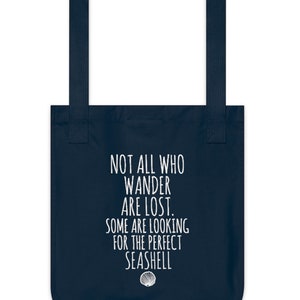May include: Navy blue tote bag with white text that reads "Not all who wander are lost. Some are looking for the perfect seashell." A white seashell icon is below the text.