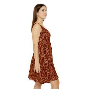 May include: A sleeveless dress featuring a repeating geometric pattern of orange and red hexagons outlined in black. The dress has a scoop neckline, a fitted bodice, and a flared skirt that falls above the knee, showcasing a consistent print.
