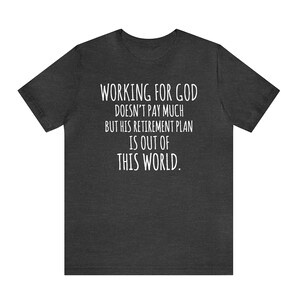 May include: Dark heather grey t-shirt with white text that reads "WORKING FOR GOD DOESN'T PAY MUCH BUT HIS RETIREMENT PLAN IS OUT OF THIS WORLD."