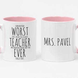May include: Two white ceramic mugs with pink interiors and handles. One mug has the text "EVEN ON YOUR WORST DAYS, YOU'RE STILL A GREAT TEACHER AND A BEAUTIFUL PERSON, DON'T YOU EVER FORGET THAT." The other mug says "MRS. PAVEL."