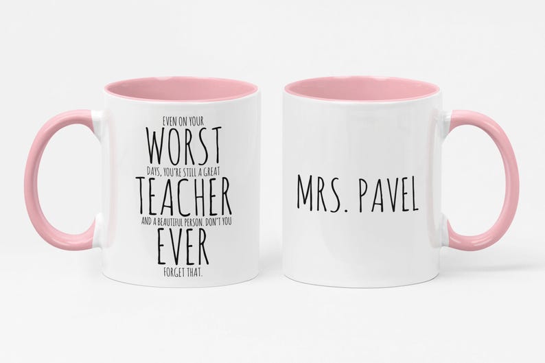 May include: Two white ceramic mugs with pink interiors and handles. One mug has the text "EVEN ON YOUR WORST DAYS, YOU'RE STILL A GREAT TEACHER AND A BEAUTIFUL PERSON, DON'T YOU EVER FORGET THAT." The other mug says "MRS. PAVEL."