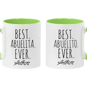 Peut inclure: Deux tasses en c&eacute;ramique blanche avec des bords verts. La tasse de gauche dit "Best Abuelita Ever." La tasse de droite dit "Best Abuelito Ever."