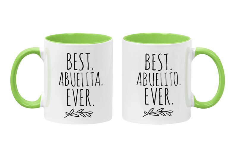 Peut inclure: Deux tasses en c&eacute;ramique blanche avec des bords verts. La tasse de gauche dit "Best Abuelita Ever." La tasse de droite dit "Best Abuelito Ever."