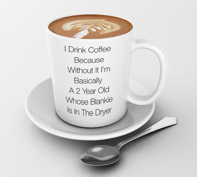 May include: White coffee mug with the text "I Drink Coffee Because Without It I'm Basically A 2 Year Old Whose Blankie Is In The Dryer" on it. The mug is filled with coffee and has a foam design on top.