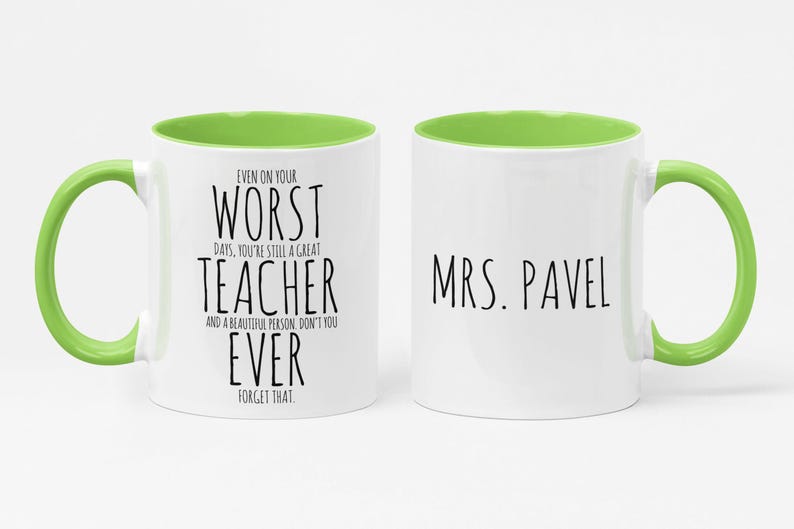 May include: White ceramic mug with a green handle and interior. The mug features the text "EVEN ON YOUR WORST DAYS, YOU'RE STILL A GREAT TEACHER" on one side and "MRS. PAVEL" on the other. A thoughtful gift for a teacher.