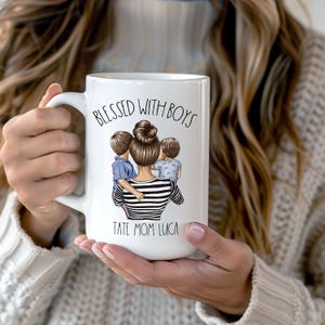 Puede incluir: Taza de cer&aacute;mica blanca con una ilustraci&oacute;n en blanco y negro de una mujer con dos ni&ntilde;os. El texto "Blessed with Boys" est&aacute; impreso en negro sobre la ilustraci&oacute;n. El texto "Tate Mom Luca" est&aacute; impreso en negro debajo de la ilustraci&oacute;n.