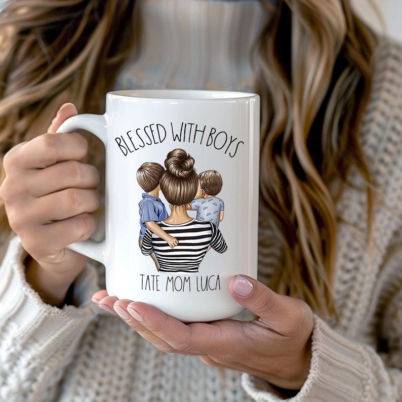 Puede incluir: Taza de cer&aacute;mica blanca con una ilustraci&oacute;n en blanco y negro de una mujer con dos ni&ntilde;os. El texto "Blessed with Boys" est&aacute; impreso en negro sobre la ilustraci&oacute;n. El texto "Tate Mom Luca" est&aacute; impreso en negro debajo de la ilustraci&oacute;n.