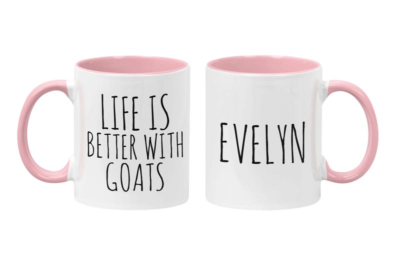 May include: Two white ceramic mugs with pink rims. One mug says "Life is better with goats" and the other mug says "Evelyn".