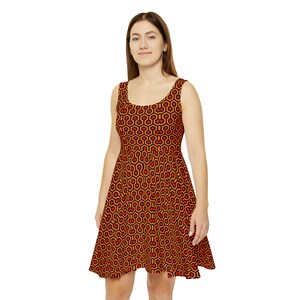 May include: A sleeveless scoop neck dress featuring a repeating geometric pattern of orange and red hexagons outlined in black. The dress has a fitted bodice and a flared skirt that falls above the knee, showcasing a consistent, bold graphic print.
