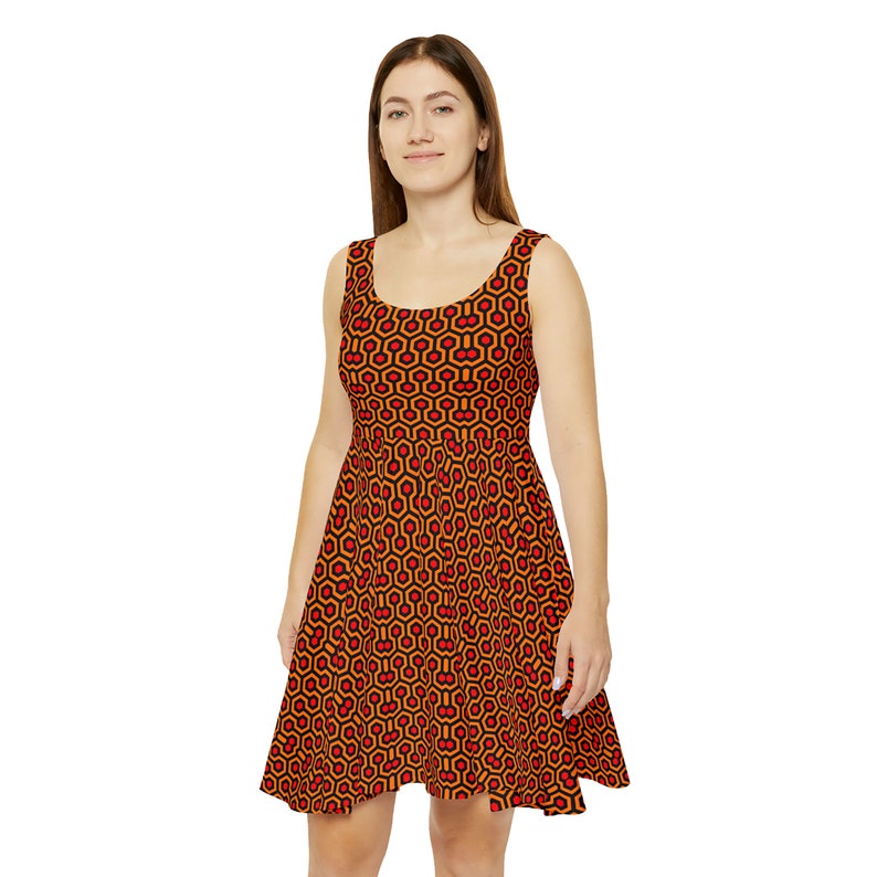 May include: A sleeveless scoop neck dress featuring a repeating geometric pattern of orange and red hexagons outlined in black. The dress has a fitted bodice and a flared skirt that falls above the knee, showcasing a consistent, bold graphic print.