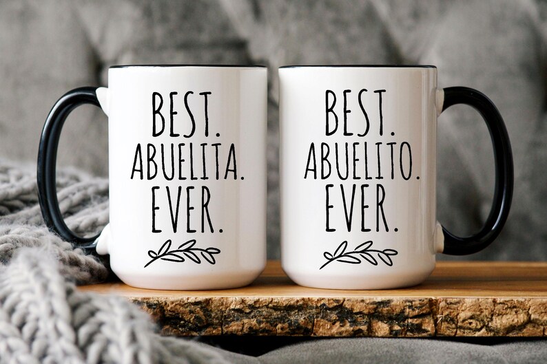 Peut inclure: Deux tasses en c&eacute;ramique blanche avec des poign&eacute;es noires et des bords noirs. La tasse de gauche dit "Best Abuelita Ever." La tasse de droite dit "Best Abuelito Ever."