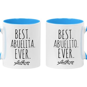 Peut inclure: Deux tasses en c&eacute;ramique blanche avec des bords et des poign&eacute;es bleus. La tasse de gauche dit "Best Abuelita Ever." La tasse de droite dit "Best Abuelito Ever."