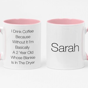 May include: White coffee mug with a pink rim and handle. The mug has text that reads "I Drink Coffee Because Without It I'm Basically A 2 Year Old Whose Blankie Is In The Dryer". The other side of the mug has the name "Sarah" in black text.