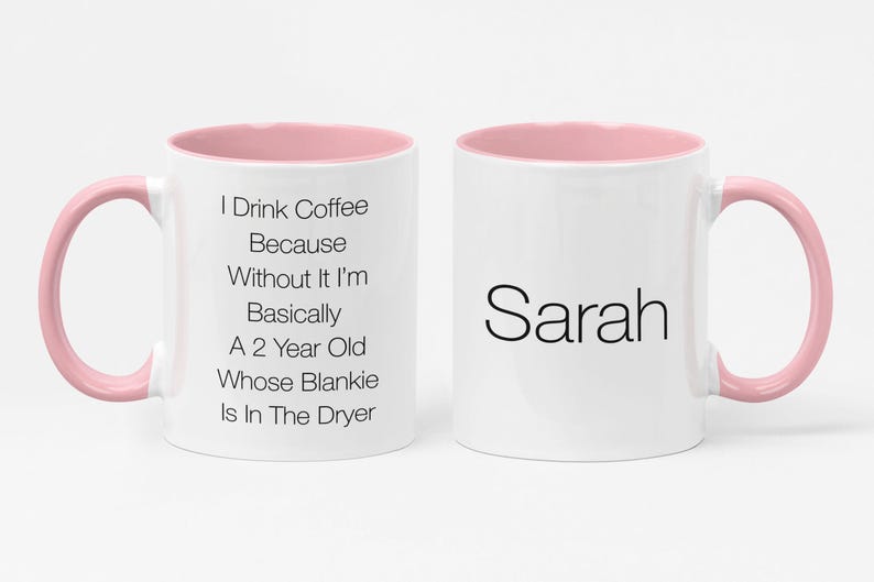 May include: White coffee mug with a pink rim and handle. The mug has text that reads "I Drink Coffee Because Without It I'm Basically A 2 Year Old Whose Blankie Is In The Dryer". The other side of the mug has the name "Sarah" in black text.