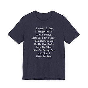 May include: Navy blue t-shirt with the text "I Came, I Saw, I Forgot What I Was Doing... And Now I Have To Pee." The text is in a white, typewriter-style font. The shirt has a crew neck and short sleeves.