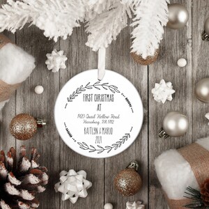 May include: White round Christmas ornament with black text that reads "First Christmas at 1420 Quail Hollow Road Harrisburg, PA 17112 Kaitlyn & Mario 2021". The ornament is surrounded by a wreath of leaves.