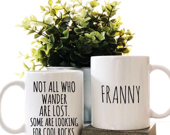 May include: Two white ceramic mugs. One mug has the text "NOT ALL WHO WANDER ARE LOST. SOME ARE LOOKING FOR COOL ROCKS." The other mug has the name "FRANNY" printed on it.