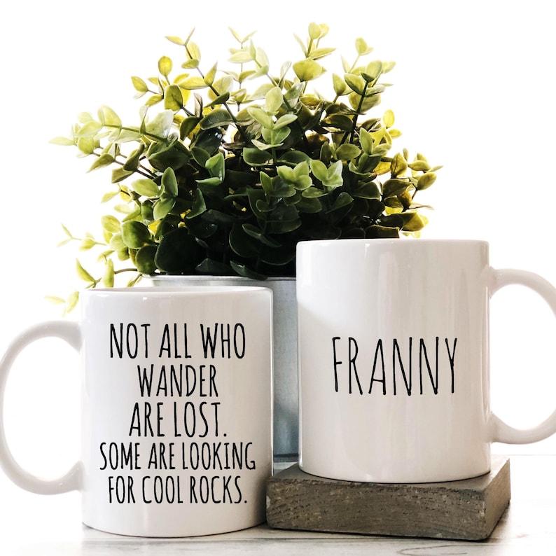 K&ouml;nnte beinhalten: Zwei wei&szlig;e Keramikbecher. Ein Becher hat den Text "NOT ALL WHO WANDER ARE LOST. SOME ARE LOOKING FOR COOL ROCKS." Der andere Becher hat den Namen "FRANNY" aufgedruckt.