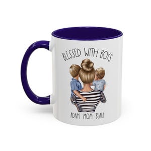 Puede incluir: Taza de cer&aacute;mica blanca con borde azul. La taza presenta un gr&aacute;fico de una mujer con dos ni&ntilde;os, con el texto "Blessed with Boys" arriba y "Adam Mom Beau" abajo.