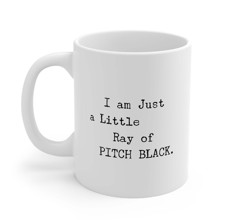 May include: White ceramic mug with black text that reads "I am Just a Little Ray of PITCH BLACK."