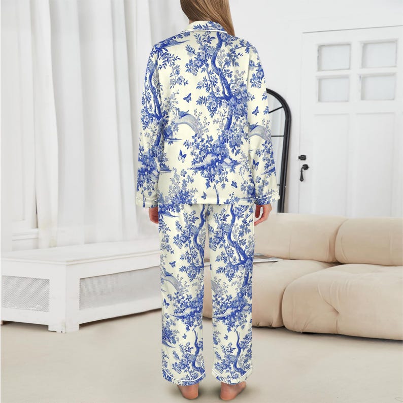 May include: A blue and white toile patterned pajama set. The long-sleeved top has a collared neckline and button closure. The matching trousers have a relaxed fit. The design includes trees, birds, and butterflies.