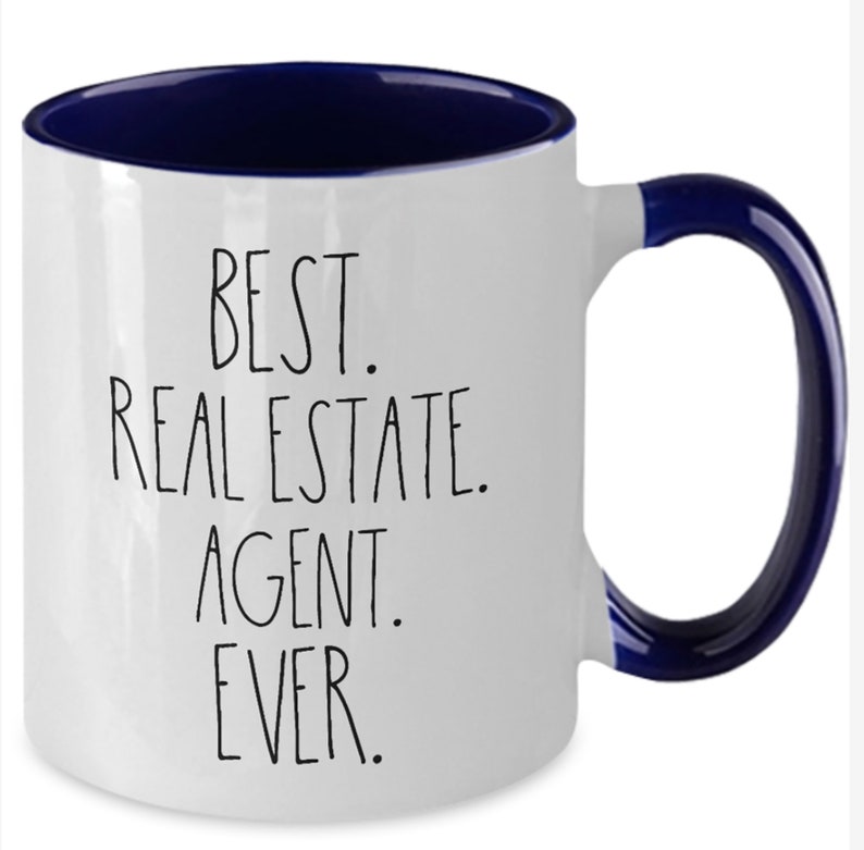 May include: White ceramic coffee mug with a blue rim and handle. The mug has black text that reads "BEST. REAL ESTATE. AGENT. EVER."