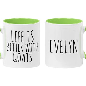 May include: Two white ceramic mugs with green rims and handles. One mug says "Life is better with goats" and the other mug says "Evelyn".
