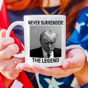 May include: White ceramic mug with a black and white image of Donald Trump and the text "Never Surrender! The Legend".