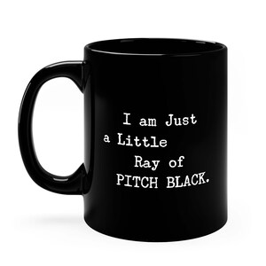 May include: Black coffee mug with white text that reads "I am Just a Little Ray of PITCH BLACK."