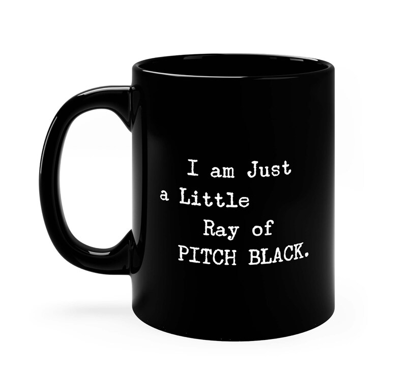 May include: Black coffee mug with white text that reads "I am Just a Little Ray of PITCH BLACK."