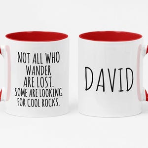 K&ouml;nnte beinhalten: Zwei wei&szlig;e Keramikbecher mit rotem Innenraum. Ein Becher tr&auml;gt den Text "NOT ALL WHO WANDER ARE LOST. SOME ARE LOOKING FOR COOL ROCKS." Der andere Becher tr&auml;gt den Namen "DAVID" aufgedruckt.