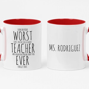 May include: White ceramic mug with a red interior and handle. The mug features the text "EVEN ON YOUR WORST DAYS, YOU'RE STILL A GREAT TEACHER" on one side and "MS. RODRIGUEZ" on the other side, in black font.