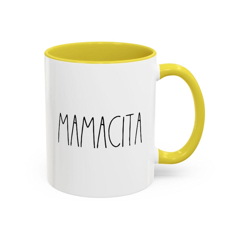 May include: White ceramic mug with a yellow interior and handle. The mug features the word "MAMACITA" in black, handwritten-style lettering. The mug is designed for hot or cold beverages.