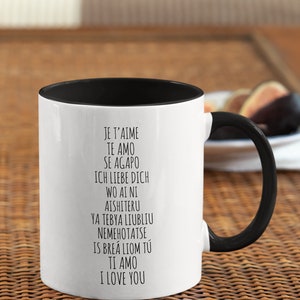 May include: White ceramic mug with a black rim and handle. The mug has black text that reads "Je t'aime, Te amo, Se agapo, Ich liebe dich, Wo ai ni, Aishiteru, Ya tebya liubliu, Nemehotatse, Is brea liom tu, Ti amo, I love you."