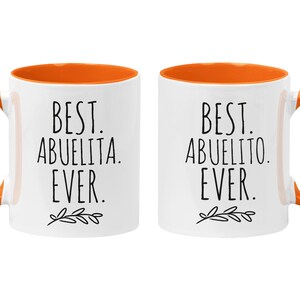 Peut inclure: Deux tasses en c&eacute;ramique blanche avec des bords orange. La tasse de gauche dit "Best Abuelita Ever." La tasse de droite dit "Best Abuelito Ever."