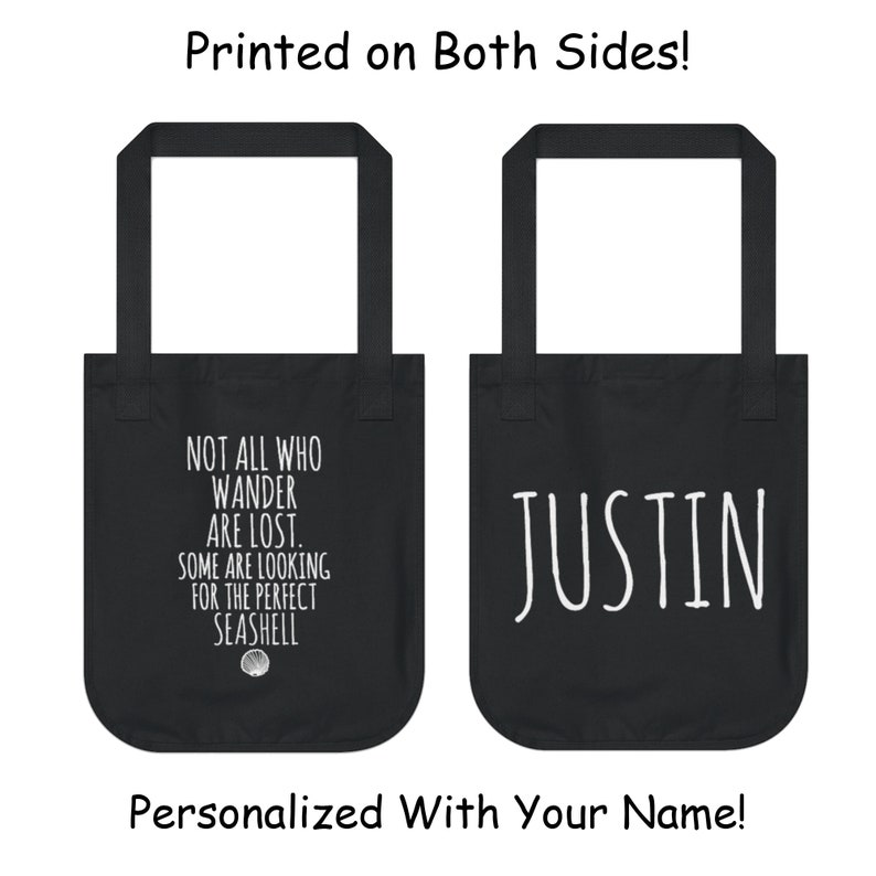 May include: Black tote bag with white text. One side says "Not all who wander are lost. Some are looking for the perfect seashell." The other side says "JUSTIN".