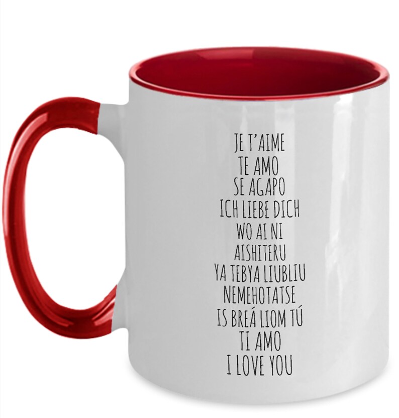 May include: White ceramic coffee mug with a red rim and handle. The mug has black text that reads "Je t'aime", "Te amo", "Se agapo", "Ich liebe dich", "Wo ai ni", "Aishiteru", "Ya tebya liubliu", "Nemehotatse", "Is bre&aacute; liom t&uacute;", "Ti amo", "I love you".