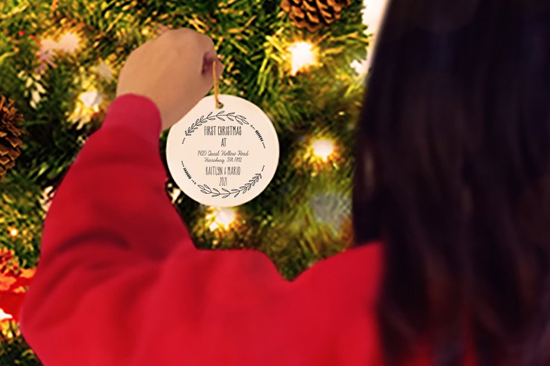 May include: A white round Christmas ornament with black text that reads "First Christmas at 1903 David Hollow Road, Harrisburg, PA 17112 Kaitlin & Mario 2021".