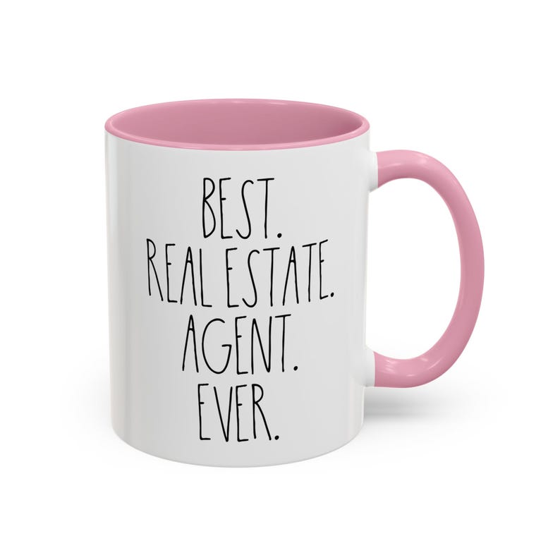 May include: White ceramic coffee mug with a pink rim and handle. The mug has black text that reads "BEST. REAL ESTATE. AGENT. EVER."