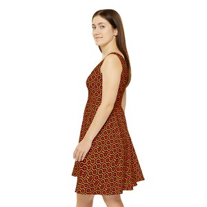 May include: A sleeveless dress featuring a repeating geometric pattern of orange and red hexagons outlined in black. The garment has a fitted bodice and a flared skirt that falls above the knee, showcasing a consistent print throughout the fabric.