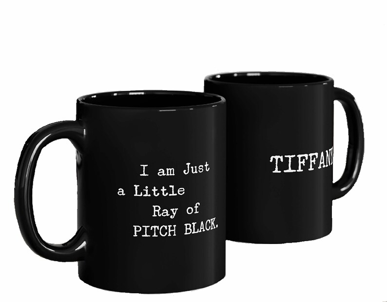 May include: Two black ceramic mugs with white text. One mug says "I am just a little Ray of PITCH BLACK." The other mug says "TIFFANY".