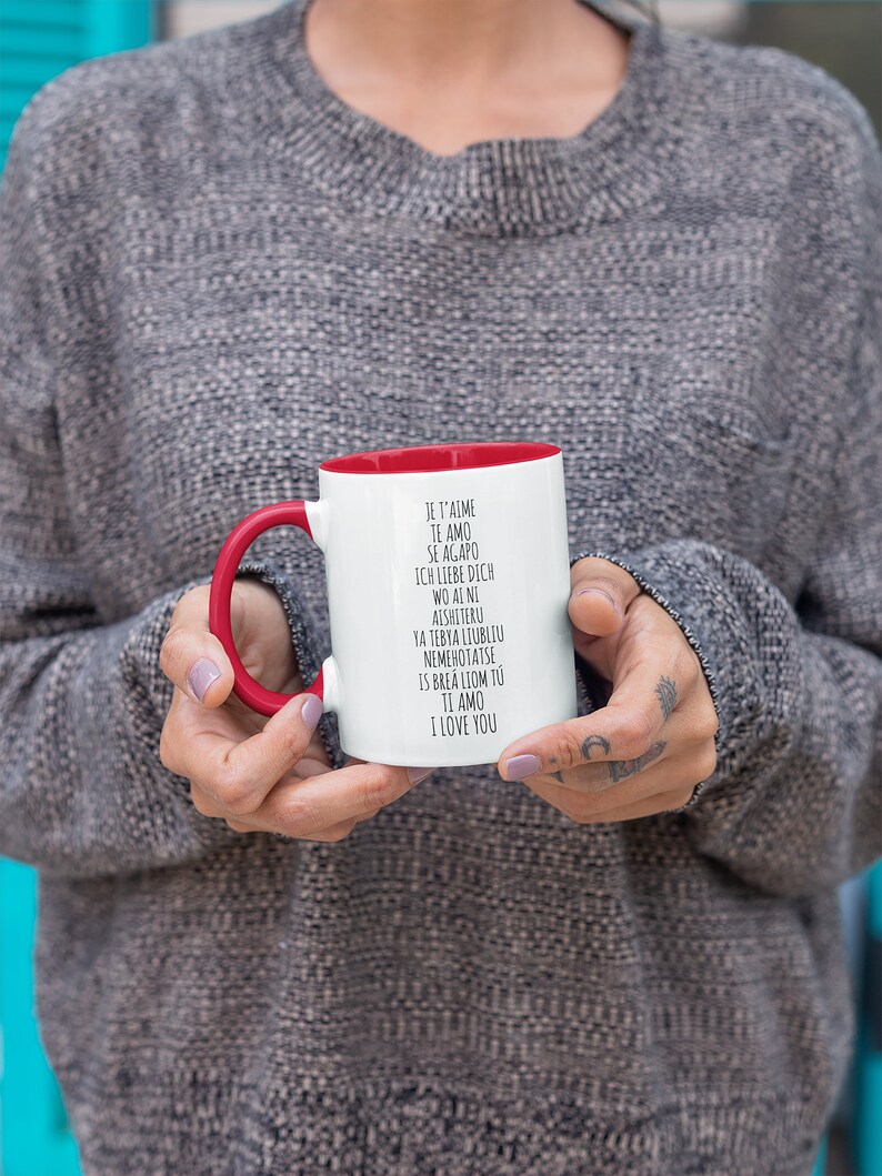 May include: White ceramic mug with a red rim and handle. The mug has black text that reads "Je t'aime, Te amo, Se agapo, Ich liebe dich, Wo ai ni, Aishiteru, Ya tebya liubliu, Nemehotatse, Is brea liom tu, Ti amo, I love you".