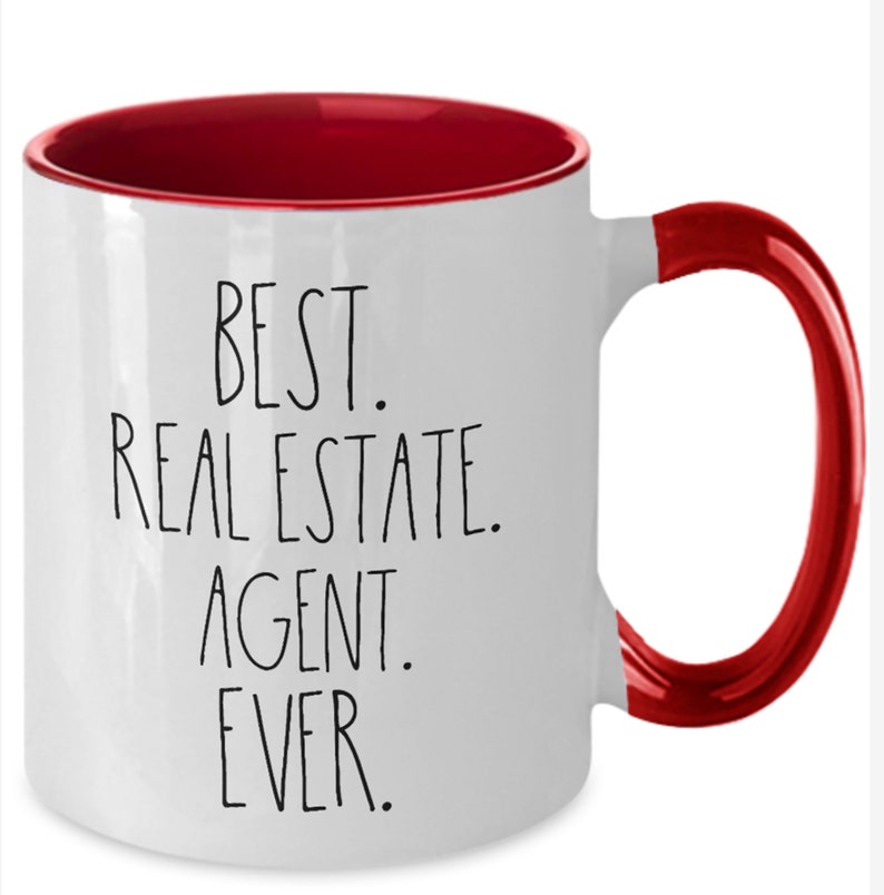 May include: White ceramic coffee mug with a red rim and handle. The mug has black text that reads "Best. Real Estate. Agent. Ever."