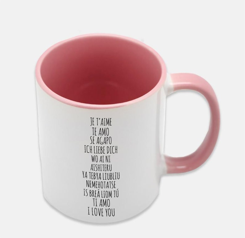 May include: White ceramic mug with a pink rim and handle. The mug has black text that reads "Je t'aime, Te amo, Se agapo, Ich liebe dich, Wo ai ni, Aishiteru, Ya tebya liubliu, Nemehotatse, Is brea liom tu, Ti amo, I love you."