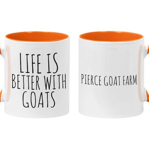 May include: A white ceramic mug with an orange rim and handle. The mug has the text "Life is better with goats" on one side and "Pierce Goat Farm" on the other side.